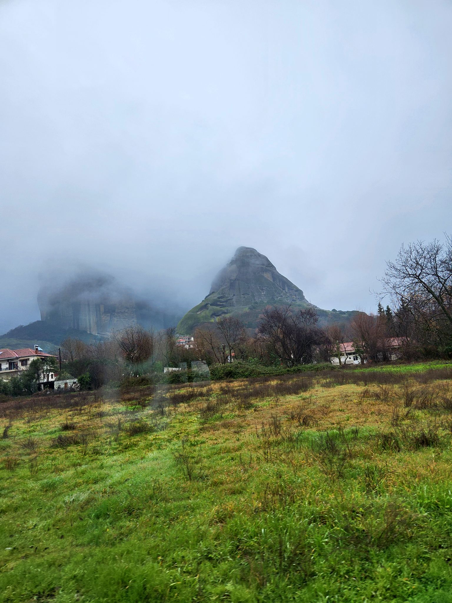Rock pillars wrapped in low cloud above a village