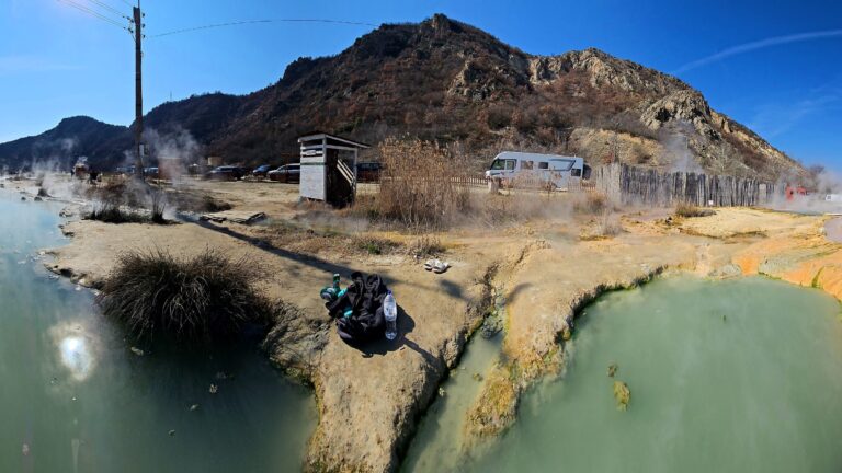 Steam rising off hot spring pools beneath a hill
